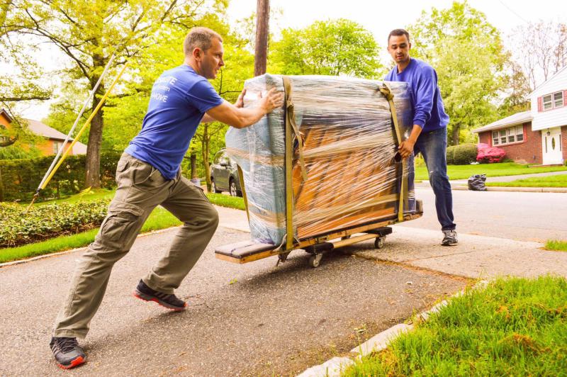 This is an image of professional movers moving some plastic wrapped furniture.